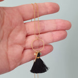 tassel necklace with black silk tassel and gold charms handheld to illustrate size