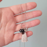 tassel necklace with black silk tassel and gold charms handheld to illustrate size